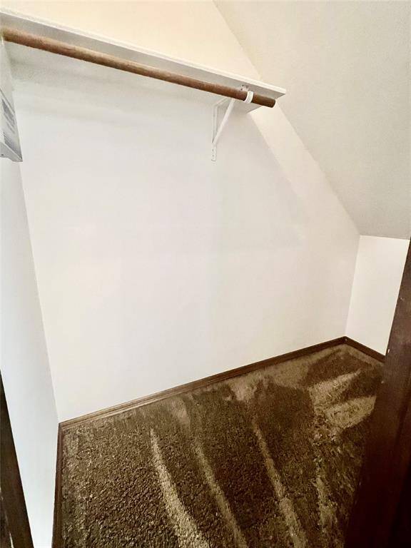 This photo shows a small, carpeted closet space with an angled ceiling and a single shelf with hanging rod, suitable for storage or wardrobe organization.