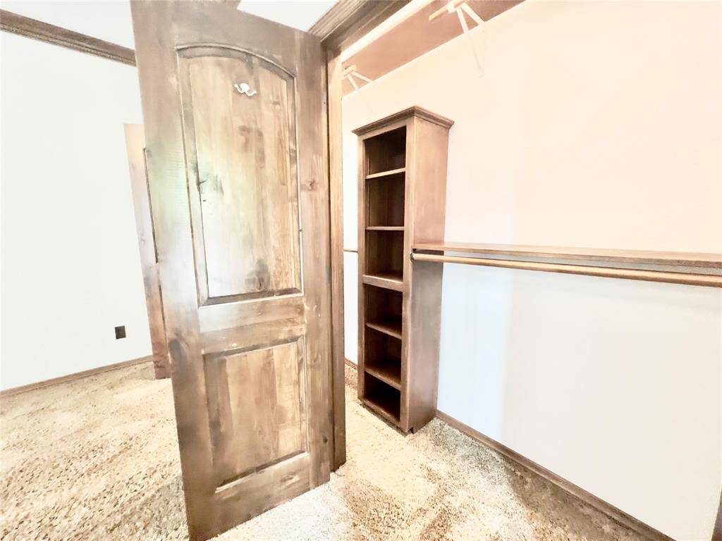 This is a room featuring a rustic wooden door, plush carpeting, and a built-in bookshelf. The space has chair rail molding and is ready for personalization.