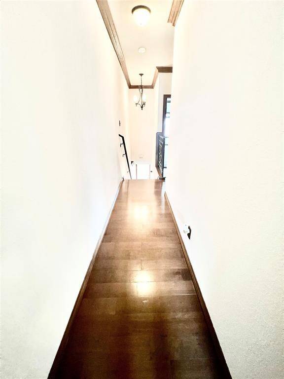 This is a well-lit, narrow hallway featuring hardwood flooring and neutral wall colors, leading to a staircase with a modern railing design. There's a ceiling light fixture and a wall sconce, adding to the ambiance.