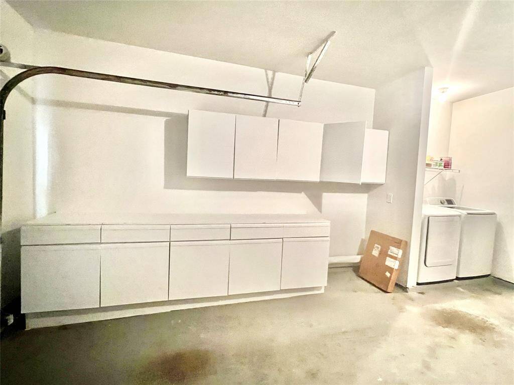This is a clean, well-lit laundry room featuring white storage cabinets, a washing machine, and ample counter space for folding clothes.