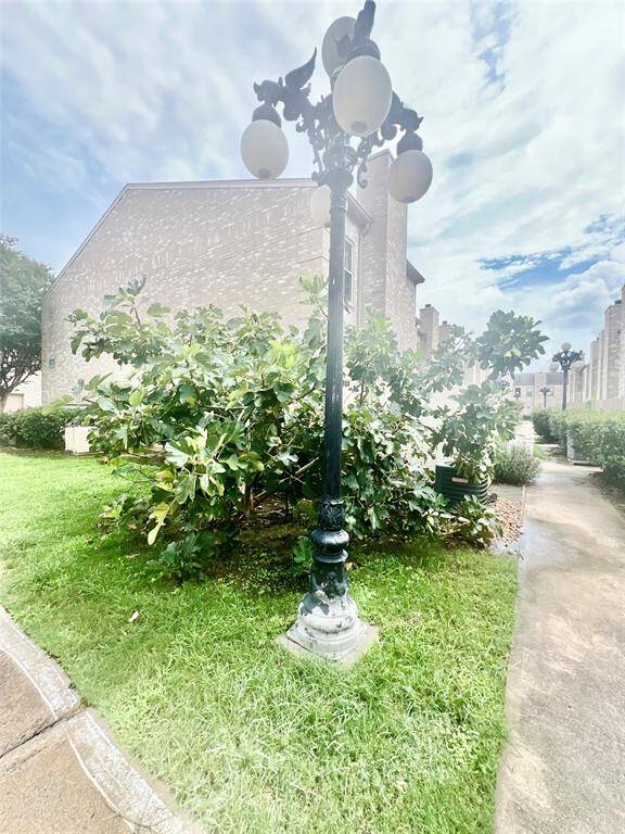 This image showcases a charming outdoor space featuring a classic street lamp surrounded by greenery, with a brick building in the background and a clear path leading through the area, suggesting a well-maintained and inviting community environment.