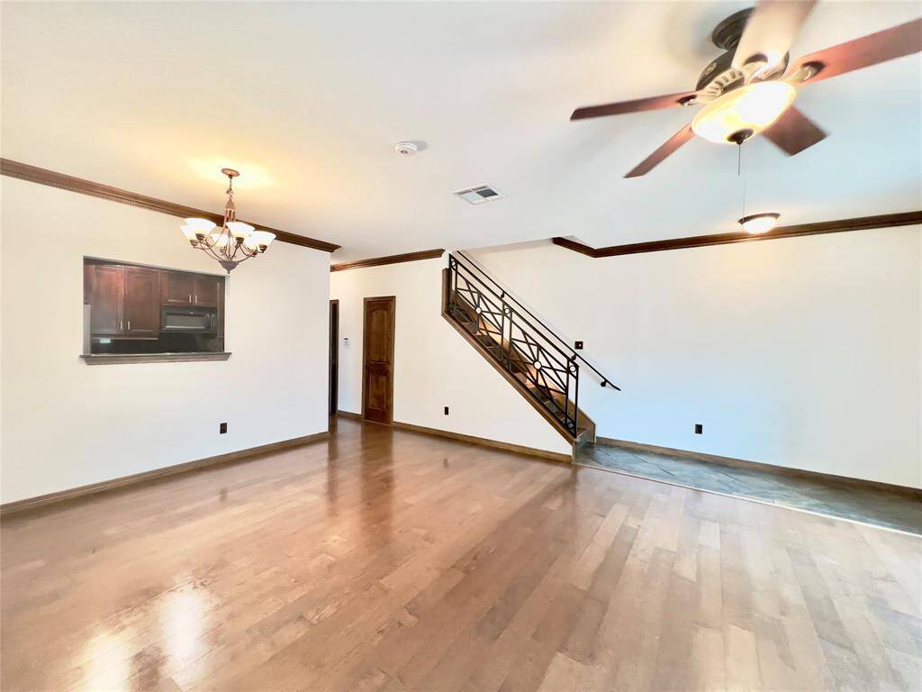This is a spacious, well-lit room with hardwood floors, featuring a ceiling fan, a chandelier, and a modern staircase leading to the upper level.