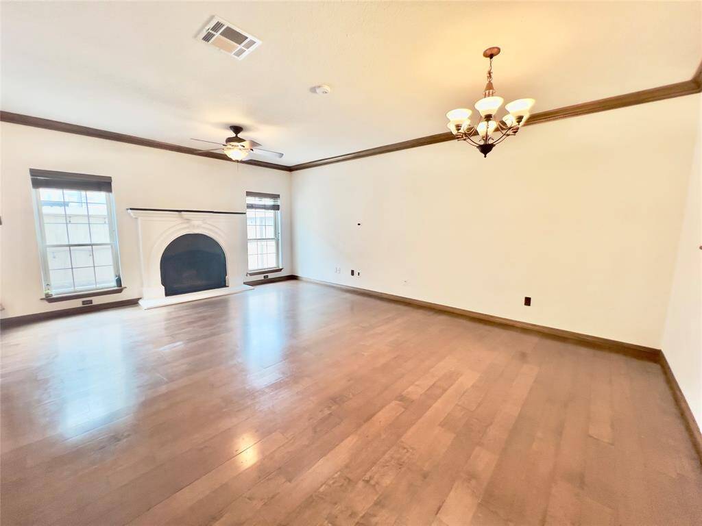 This is a spacious living area featuring hardwood floors, a central fireplace, large windows, and ceiling fans, with plenty of natural light.
