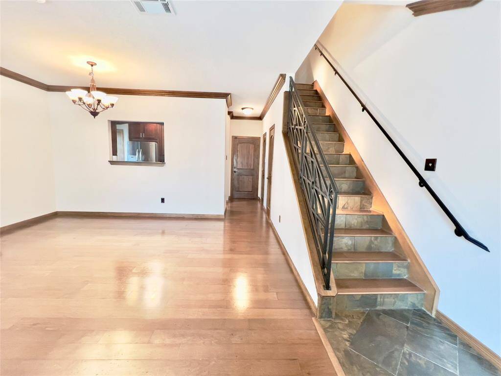You're viewing a spacious room with hardwood flooring, featuring an elegant chandelier, a staircase with decorative metal railings, and a pass-through window to another room. The area is well-lit and ready for personalization.