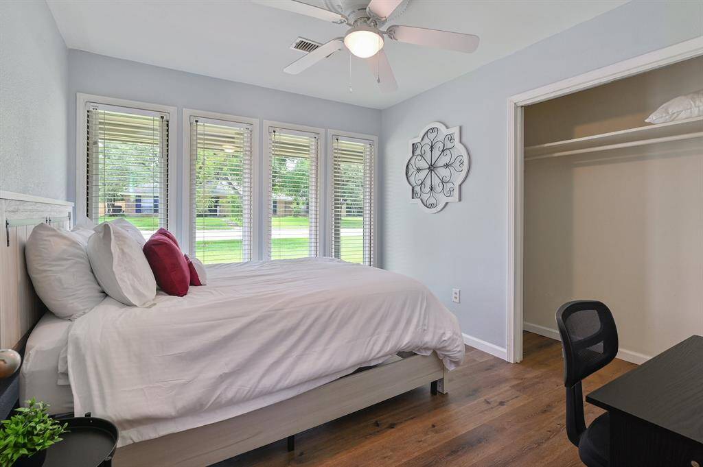 Multiple windows line one wall, bathing this bedroom in natural light. A generously sized closet provides ample storage, while a ceiling fan with an integrated light fixture ensures comfort.