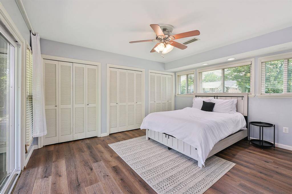 The primary bedroom is a spacious and serene retreat featuring a ceiling fan, recessed lighting, and a soothing neutral color scheme. Multiple windows span a wall, inviting in soft natural light. Sliding glass doors provide direct access to the backyard while offering a scenic view. Ample closet space ensures organization, and the en suite bath adds an extra layer of comfort.