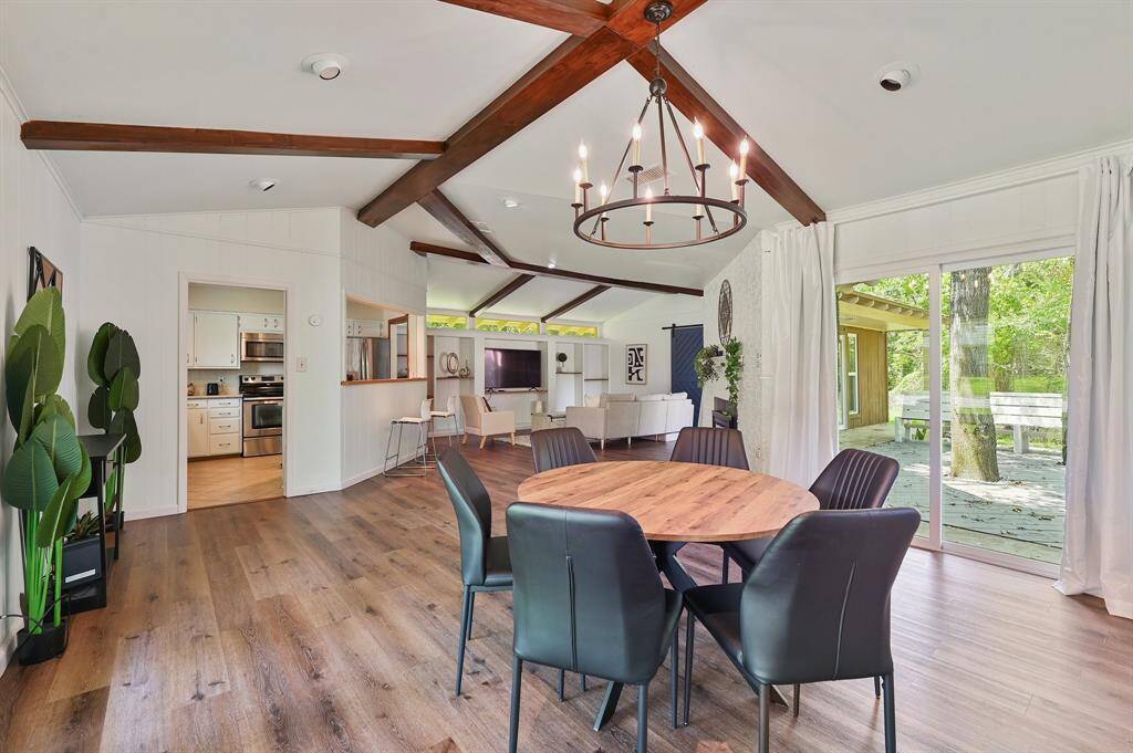 The dining area is a bright and inviting space featuring warm wood-like laminate flooring that adds a touch of elegance. Sliding glass doors offer a seamless connection to the outdoors, filling the room with natural light and providing a picturesque view. Opposite, multiple large windows stretch across the wall, enhancing the airy atmosphere. The open layout provides a clear view of the living room, while the kitchen remains easily accessible through a doorway.