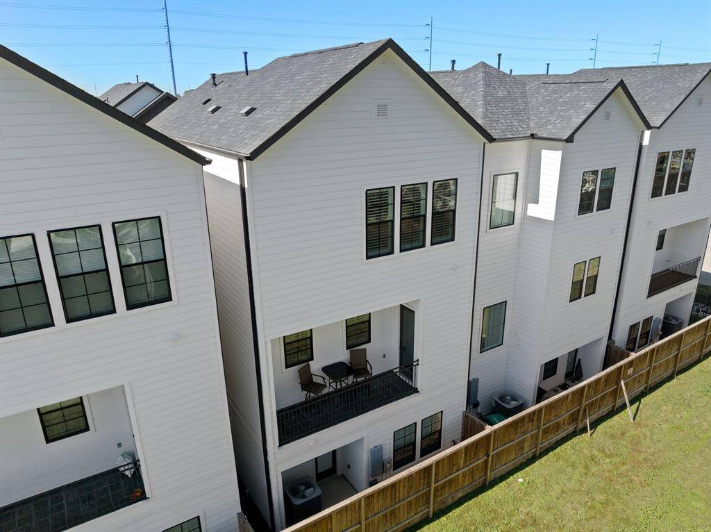 A view of the back side of the home featuring both its covered backyard space as well as the covered second floor balcony looking out to the green space behind.