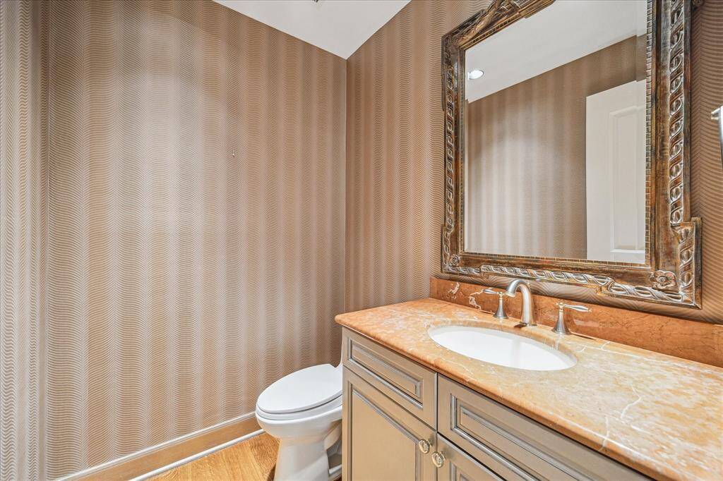 Elegantly wallpapered powder room with marble countertop and under counter storage.