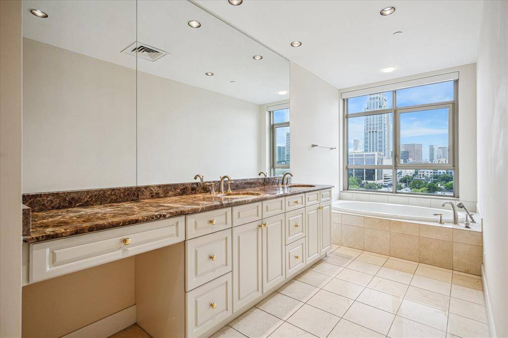 Primary bathroom with separate, jetted spa-like bathtub, double sinks, vanity, a separate shower with ample under counter storage cabinets with natural sunlight coming through the large windows next to bathtub.