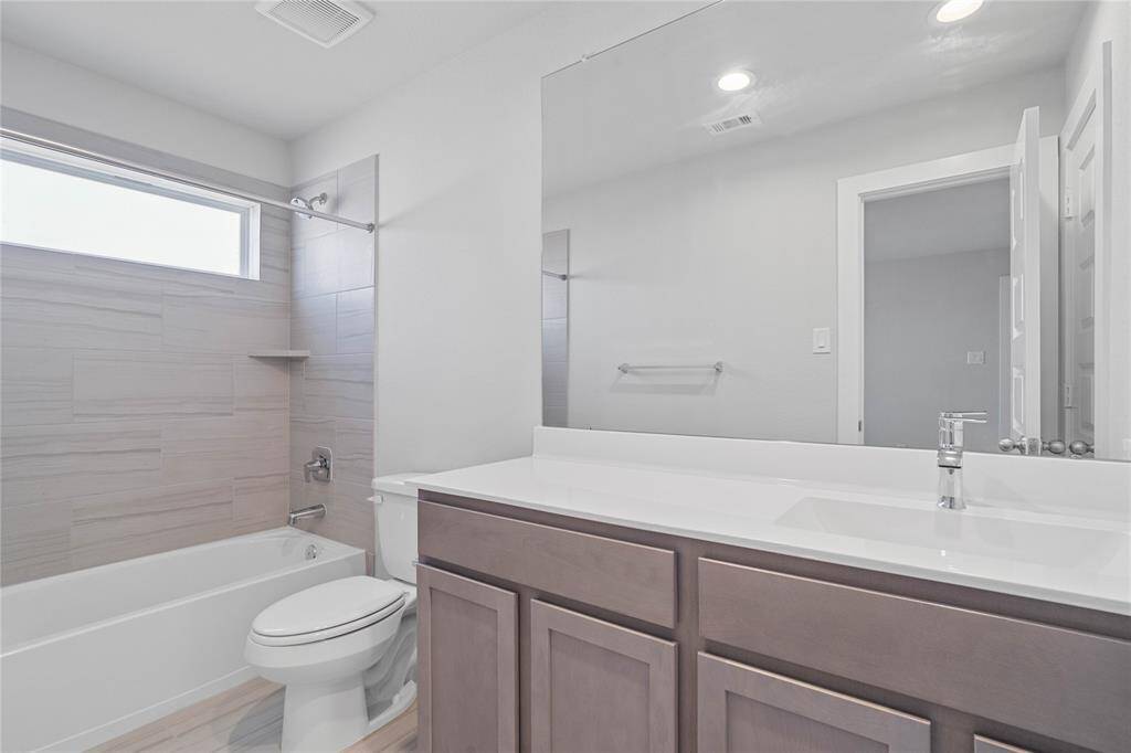 Secondary bath features tile flooring, bath/shower combo with tile surround, stained wood cabinets, beautiful light countertops, mirror, sleek fixtures and modern finishes.