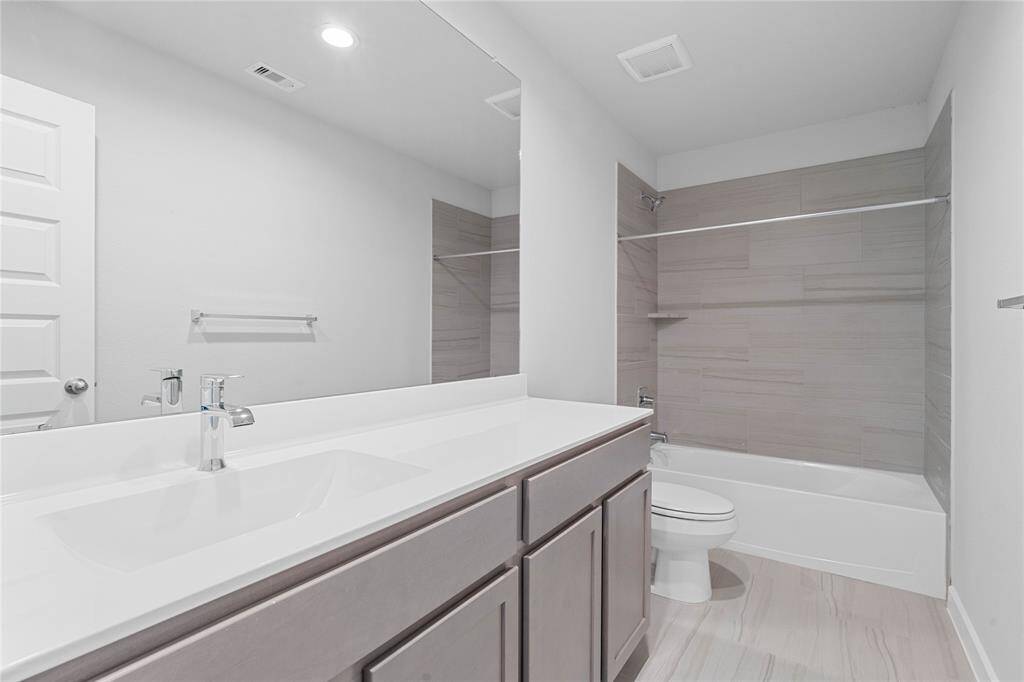 Secondary bath features tile flooring, bath/shower combo with tile surround, stained wood cabinets, beautiful light countertops, mirror, sleek fixtures and modern finishes.