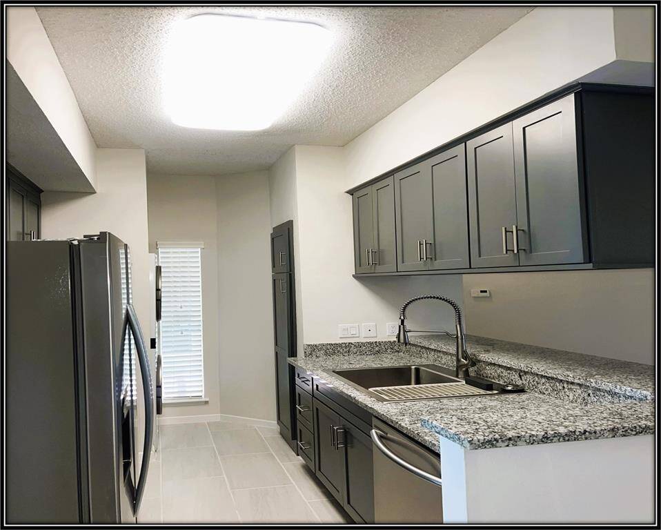 Modern kitchen with sleek gray cabinetry, granite countertops, and stainless steel appliances. Bright lighting and a compact, efficient layout make it ideal for cooking and entertaining.
