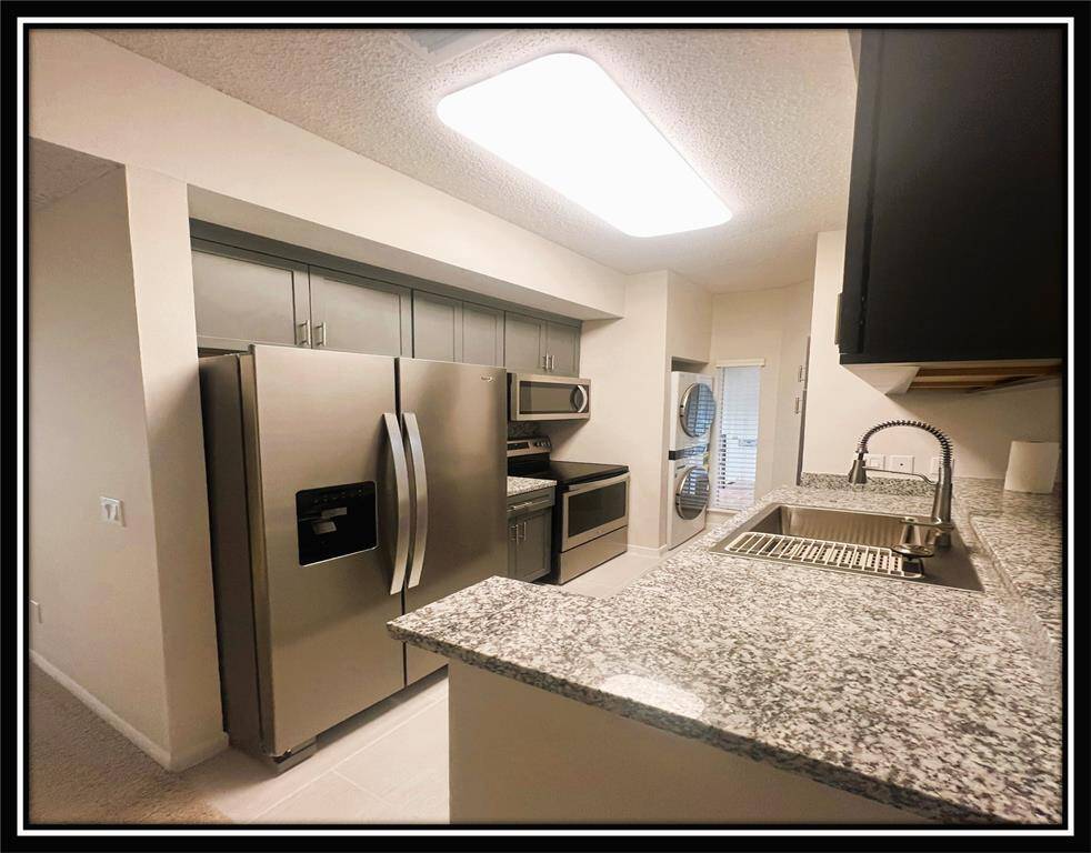 Modern kitchen with granite countertops, stainless steel appliances, and ample cabinetry. Includes a stacked washer and dryer in a compact layout. Bright lighting enhances the space.