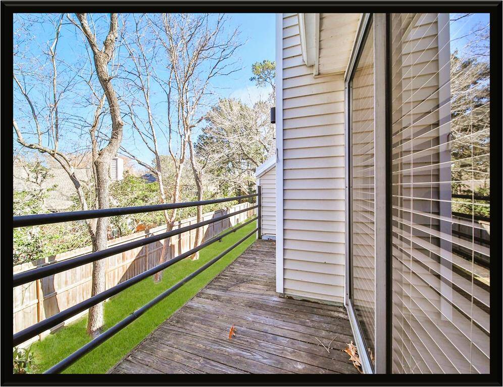 This photo showcases a narrow wooden deck alongside the condo, featuring large windows with coverings. The area is bordered by a fence, with a view of trees and a neatly maintained lawn, creating a serene and private outdoor space.