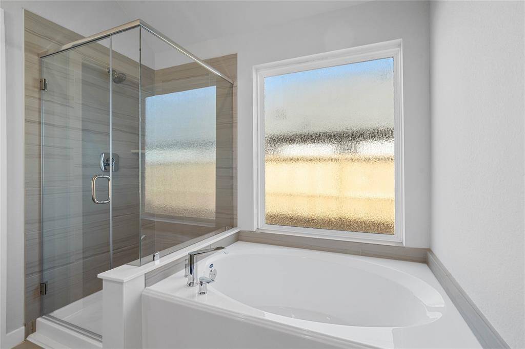 Additional view of the primary bathroom features a dark framed walk-in shower with tile surround, separate garden tub for soaking after a long day, and gorgeous tempered glass windows to allow in the natural light!