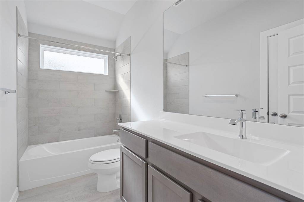 Secondary bath features tile flooring, bath/shower combo with tile surround, stained wood cabinets, beautiful light countertops, mirror, dark, sleek fixtures and modern finishes!