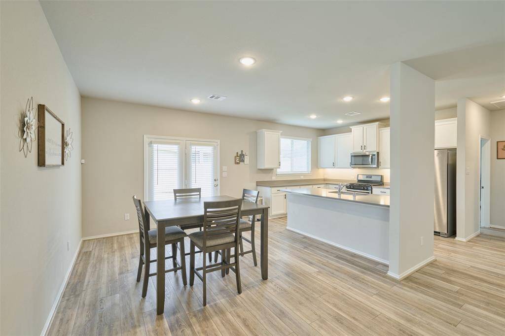 Bright and spacious open-concept kitchen and dining area featuring modern stainless steel appliances, sleek white cabinetry, wood flooring, and a cozy dining nook with ample natural light.
