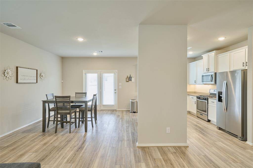 This photo showcases a modern, open-concept kitchen and dining area. It features sleek stainless steel appliances, white cabinetry, and light wood flooring. The dining space has a set of glass doors leading outside, providing plenty of natural light.
