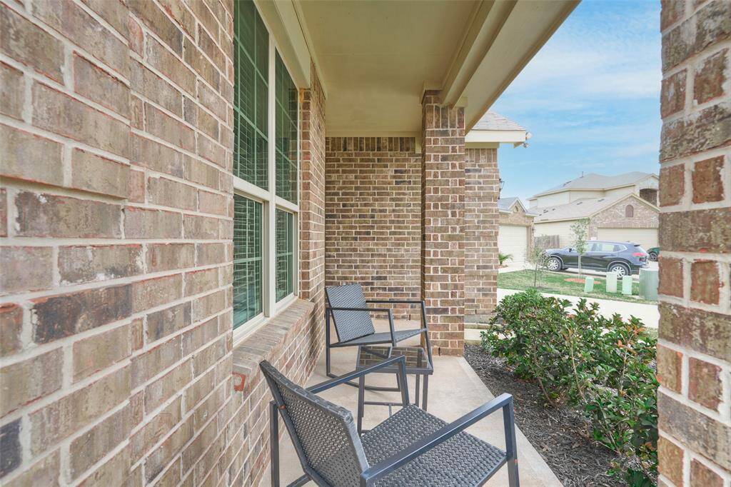 This photo showcases a charming brick front porch with seating, offering a cozy outdoor space. It features a view of a well-maintained neighborhood and a small garden area, perfect for relaxing.