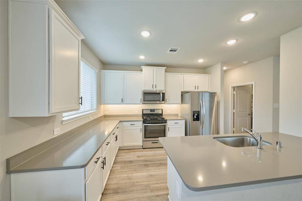 Bright, modern kitchen with stainless steel appliances, sleek countertops, and ample white cabinetry. Features a center island with a sink and recessed lighting, offering a clean and spacious feel.