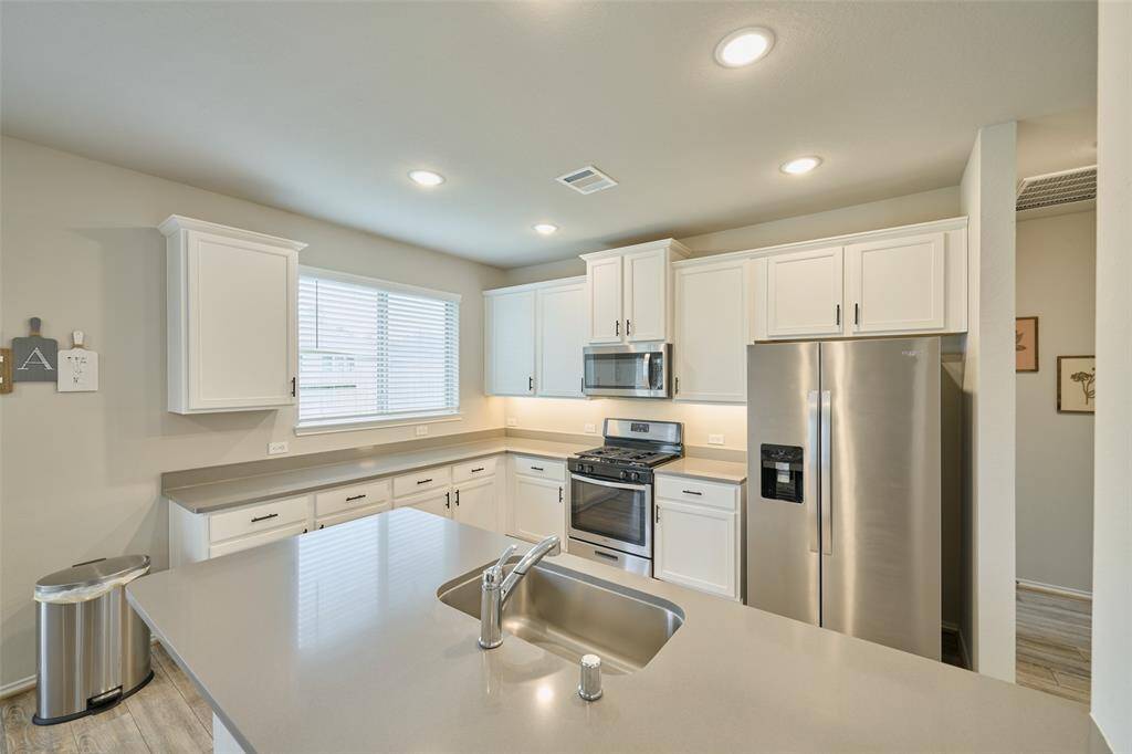 This modern kitchen features sleek stainless steel appliances, white cabinetry, and a spacious island with a sink. The neutral countertops and ample lighting create a bright and inviting space, perfect for cooking and entertaining.