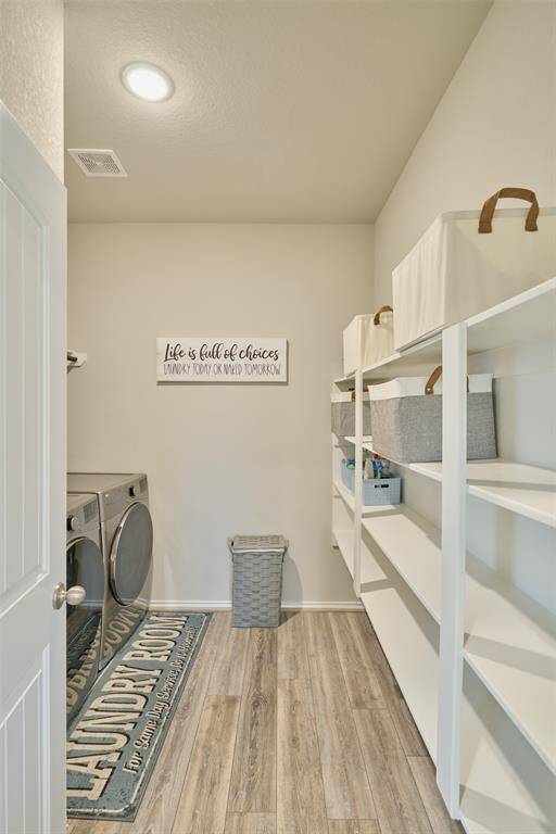 This photo showcases a bright, organized laundry room featuring modern appliances, ample shelving for storage, and stylish decor. The space is well-lit with a clean, minimalist design, offering functionality and convenience.