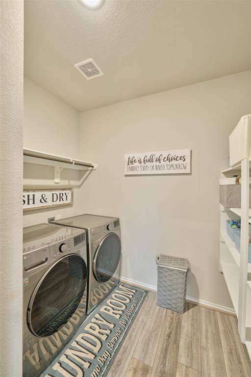 This laundry room features modern appliances, a wall-mounted drying rack, and ample shelving. It has a cozy atmosphere with light wood flooring and cheerful decor.