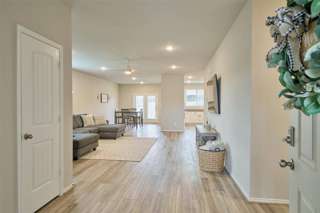 This photo showcases a bright, open-concept living area with wood flooring. It includes a cozy sectional sofa, a dining area, and a modern kitchen in the background. The space is inviting and well-lit, with neutral tones and stylish decor.