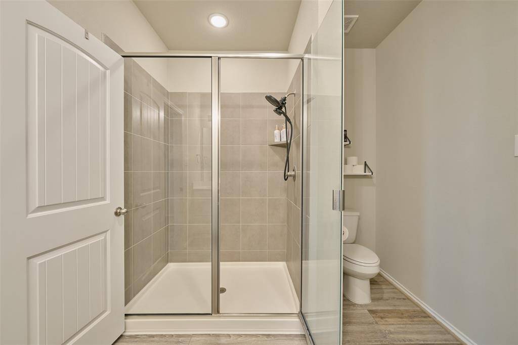 This bathroom features a modern shower with glass doors and sleek tilework. Adjacent is a toilet with a convenient shelf for essentials. The space is well-lit, and the neutral tones create a clean, inviting atmosphere.