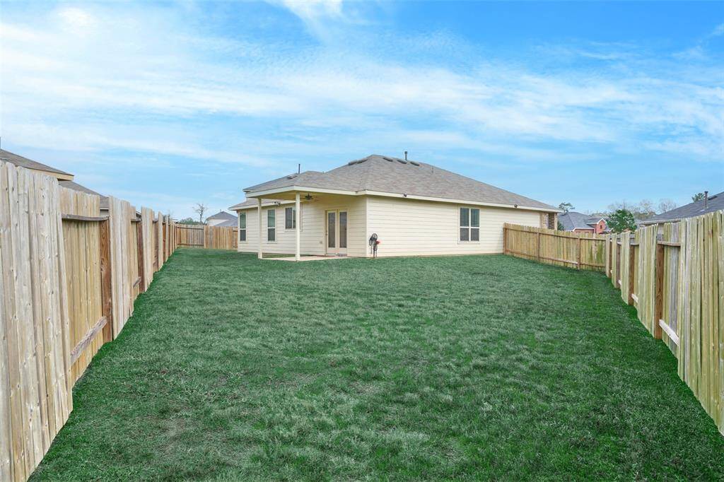 Spacious backyard with well-maintained grass and a wooden fence for privacy. The house features a covered patio, ideal for outdoor gatherings.