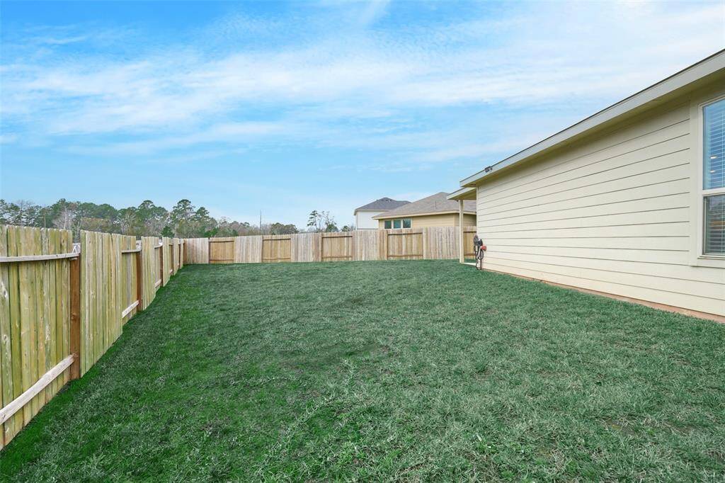 Spacious backyard with well-maintained grass, enclosed by a wooden fence for privacy, adjacent to a light-colored house. Ideal for outdoor activities and relaxation.