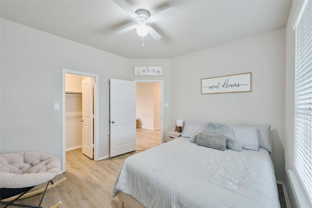 This is a cozy bedroom featuring a comfortable bed, soft neutral colors, and natural light from a large window. It includes a ceiling fan, a small sitting area, and a walk-in closet, creating a welcoming and functional space.