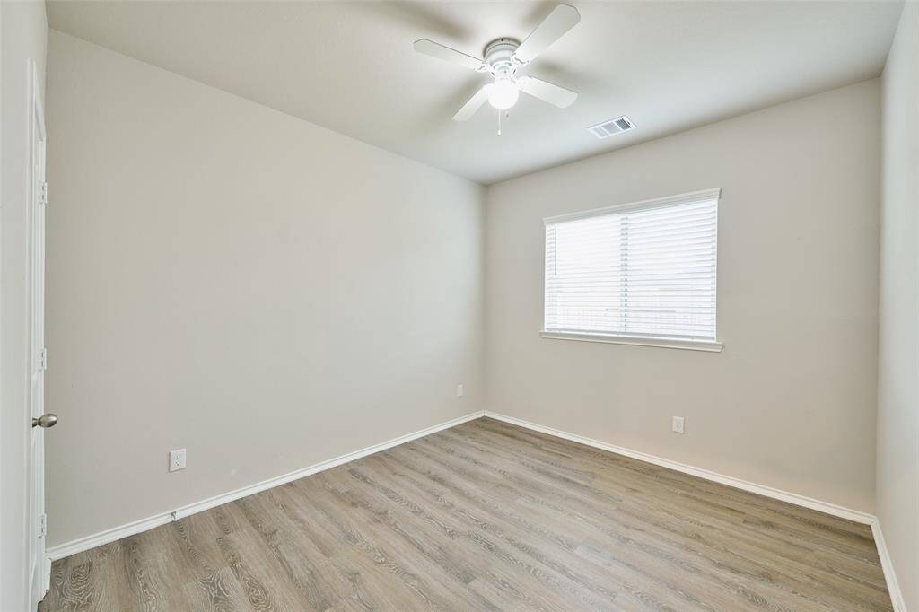 This room features neutral walls and wood-style flooring, creating a clean and modern feel. It includes a window with blinds for natural light and a ceiling fan for comfort.