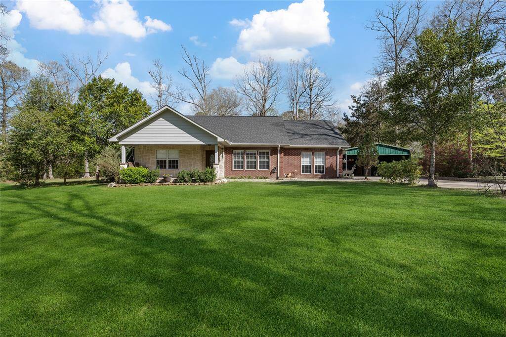 Charming single-story brick home with a large, well-maintained lawn and mature trees. The house features a covered porch and a carport, offering ample space for outdoor activities in a serene, natural setting.