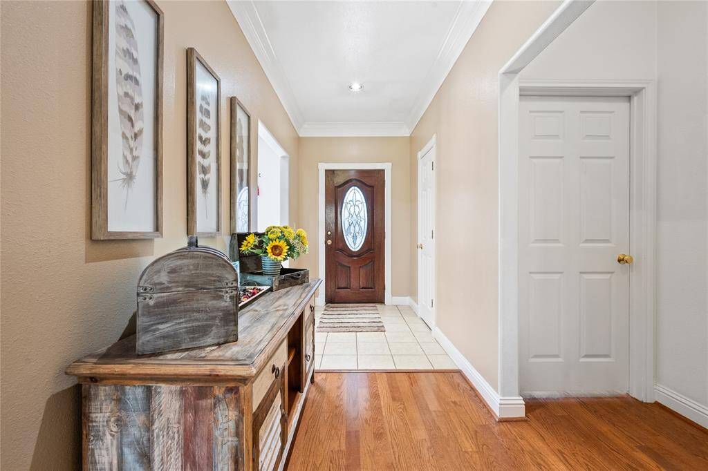 This inviting entryway features warm wood floors with decorative accents, and a stylish front door with glass detailing. Light walls and crown molding add a touch of elegance.