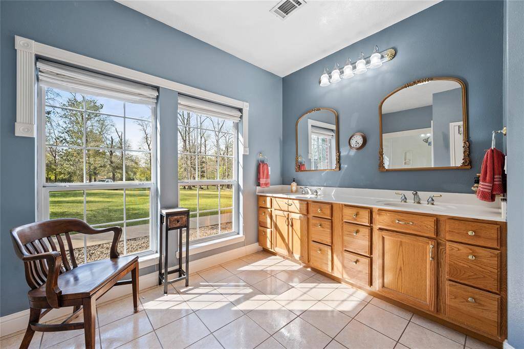 The primary bathroom features large windows with scenic views, a long double vanity with ample storage, elegant mirrors, all enhanced by a soothing blue color scheme.