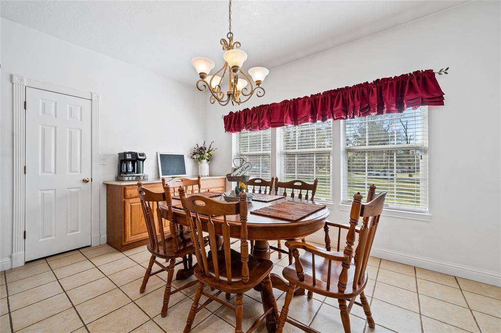 This bright dining area features a tasteful chandelier, and large windows with red valances, offering plenty of natural light and a welcoming view of the outdoors.
