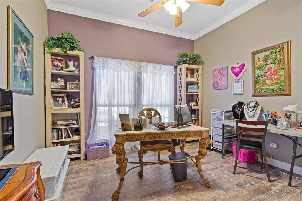 The side secondary bedroom is currently being utilized as office space. The room features wood-like tile flooring, tall baseboards, crown molding, and a ceiling fan.