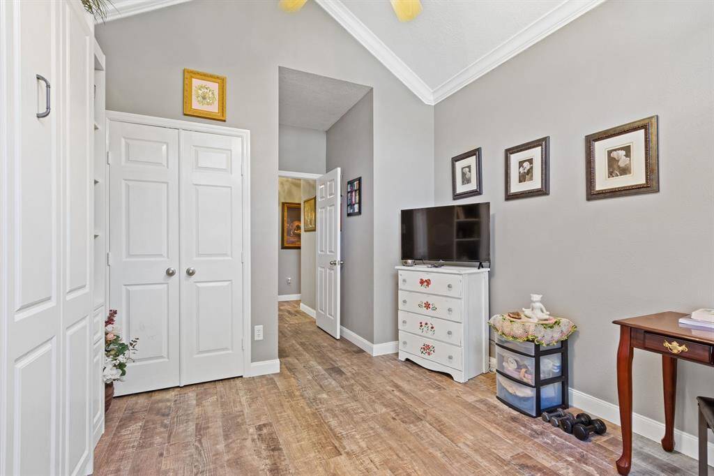 This secondary bedrooms offers a tall ceiling in addition to wood-like tile, tall baseboards, crown molding, and a ceiling fan.