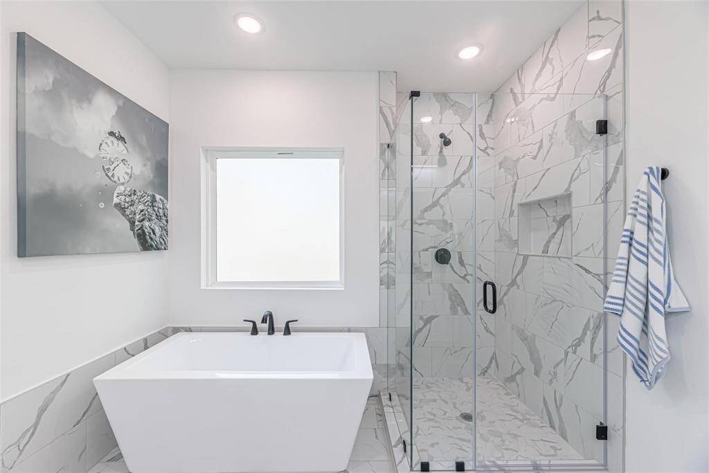 This modern bathroom features a sleek freestanding bathtub, a spacious glass-enclosed shower with elegant marble tile, and contemporary fixtures, creating a luxurious spa-like ambiance.