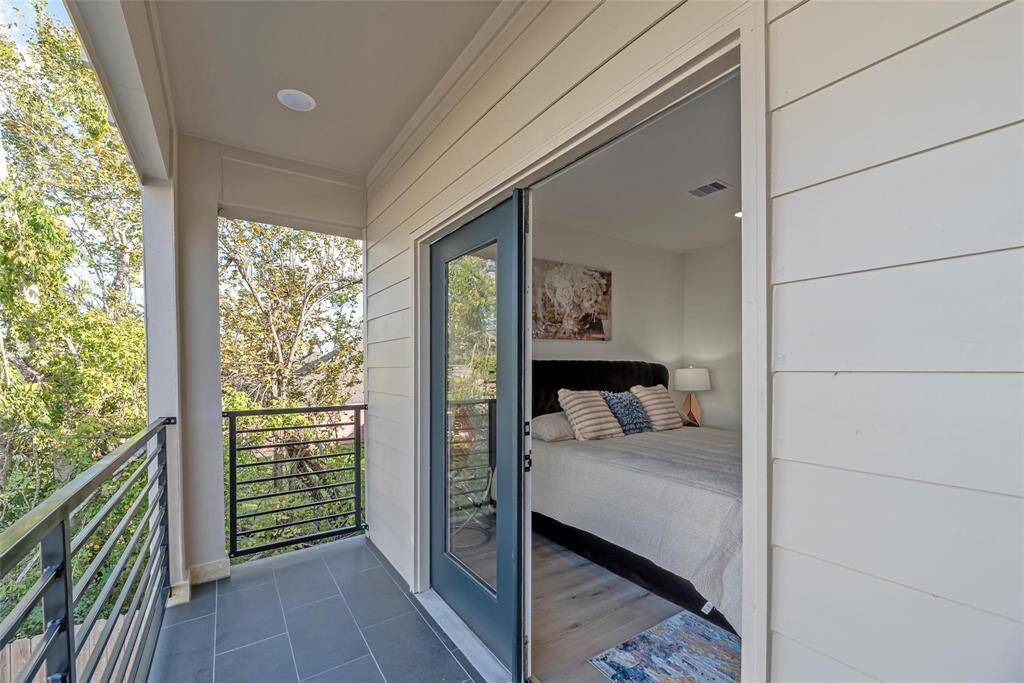This image displays a comfortable bedroom that has access to a balcony. With its contemporary railing and view of beautiful trees, the balcony connects the bedroom to a tranquil outside area.