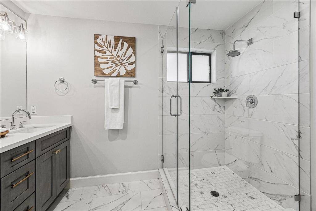This spa-like ensuite bathroom also offers the convenience and comfort of an oversized walk-in shower, featuring a luxurious rain shower head, stunning tile work, and a sleek frameless glass enclosure.