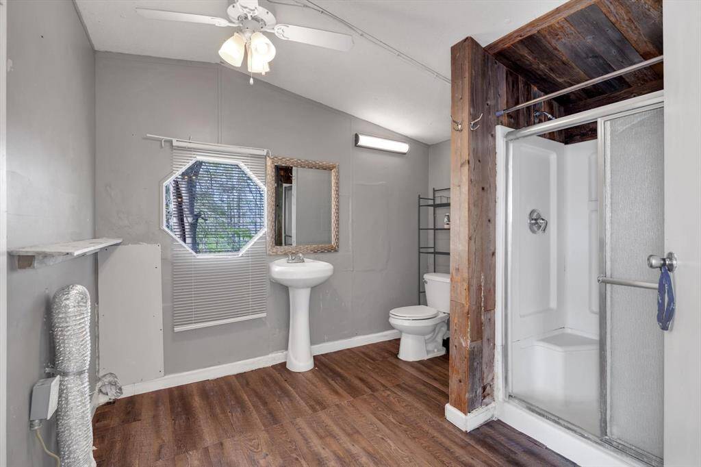 Spacious primary bathroom featuring a modern shower, elegant pedestal sink, and stylish wood accents, all enhanced by natural light from a unique octagonal window.