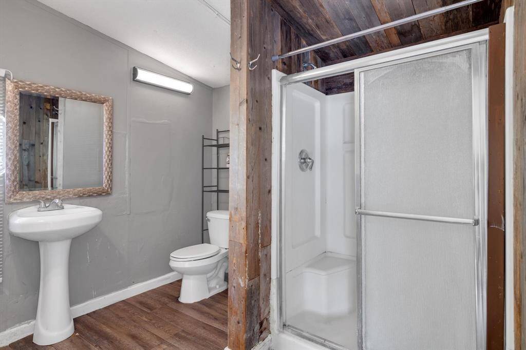 This bathroom features a rustic design with wood look accents, a modern pedestal sink, and a shower with sliding glass doors. The space is compact yet functional, with a neutral color scheme and a large mirror.