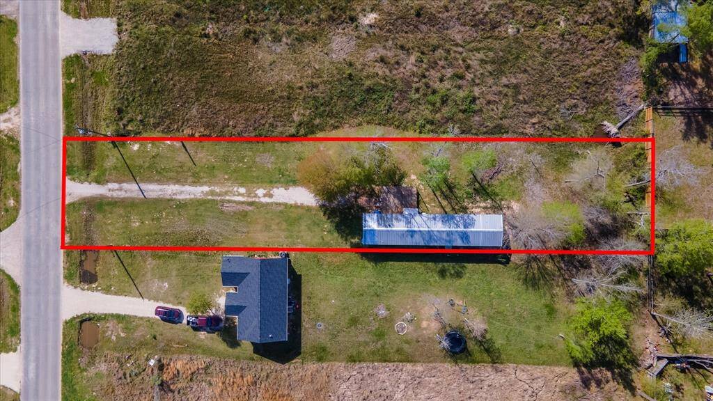 Rectangular plot of land bordered in red. It features a mobile house with a driveway and yard, surrounded by open grass and some trees. The property is adjacent to a road, suggesting easy access.