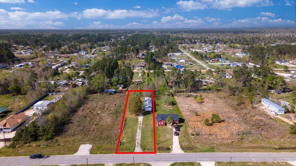 Property outlined in red, featuring a long driveway leading to a house. The home is surrounded by open land with scattered trees, set in a peaceful, semi-rural neighborhood with other homes nearby.