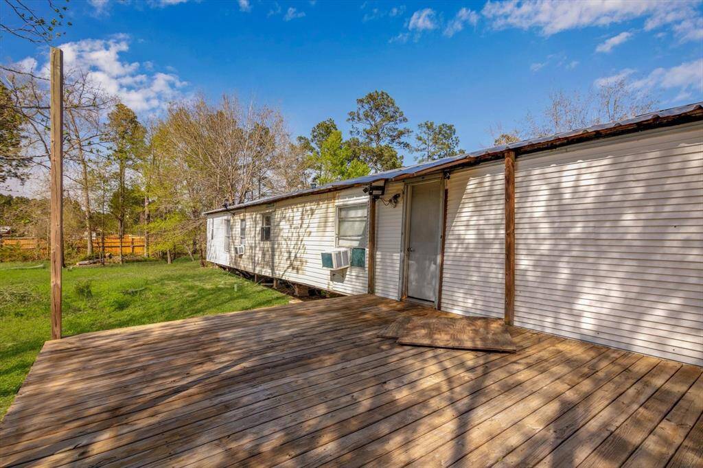 Mobile home with a spacious wooden deck, set in a grassy yard with surrounding trees, perfect for outdoor relaxation.