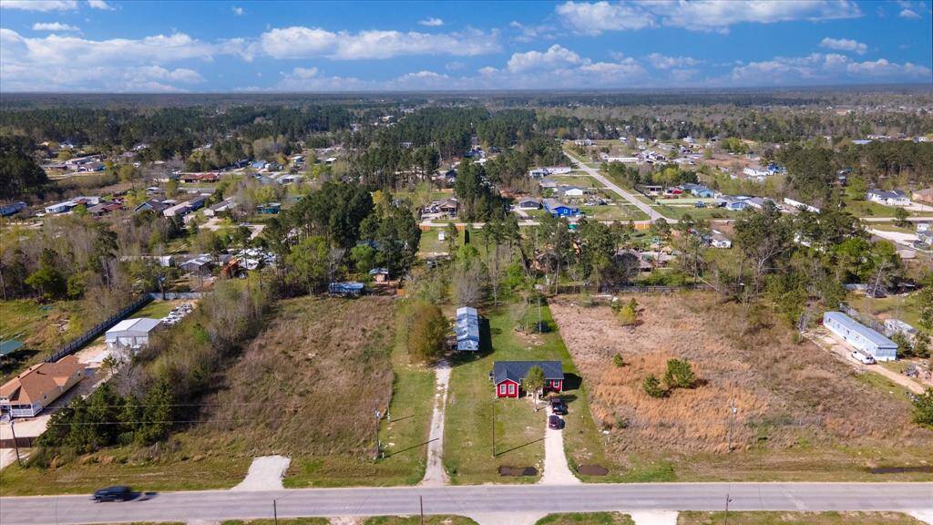 This aerial photo showcases a rural property with a long driveway, surrounded by open land and scattered trees. The neighborhood features spacious lots and a mix of homes, offering a peaceful, natural setting.