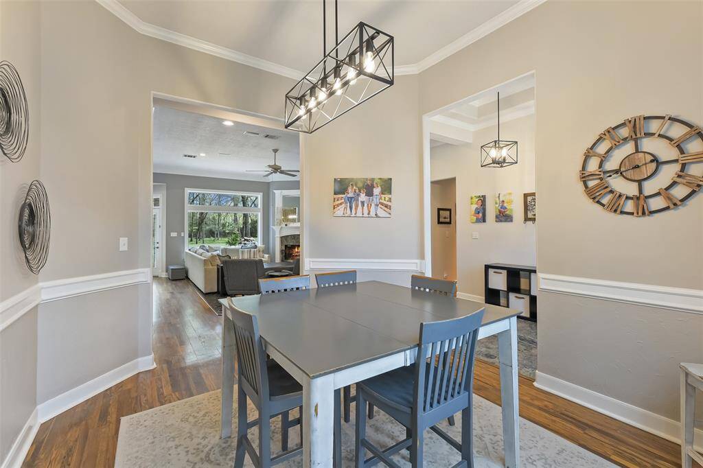 This dining room features elegant wainscoting, a modern chandelier, and a neutral color palette. Wall decor adds a personal touch, and the space opens into a bright living area with hardwood floors.